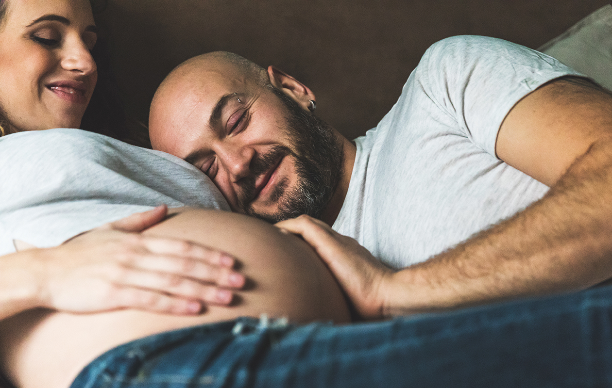 un homme a la main et la tête tout contre le ventre d'une femme enceinte