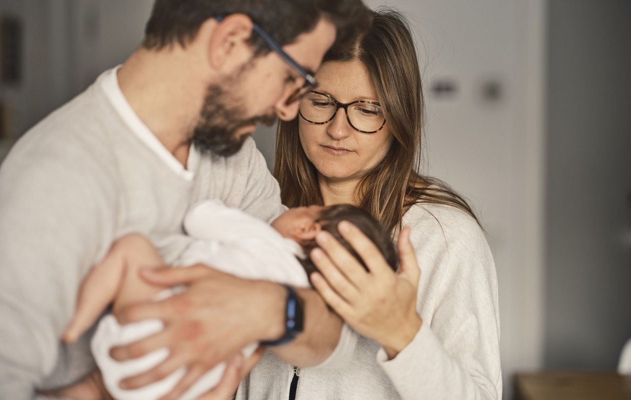 de jeunes parents regardent leur nourrisson tenu dans les bras du père