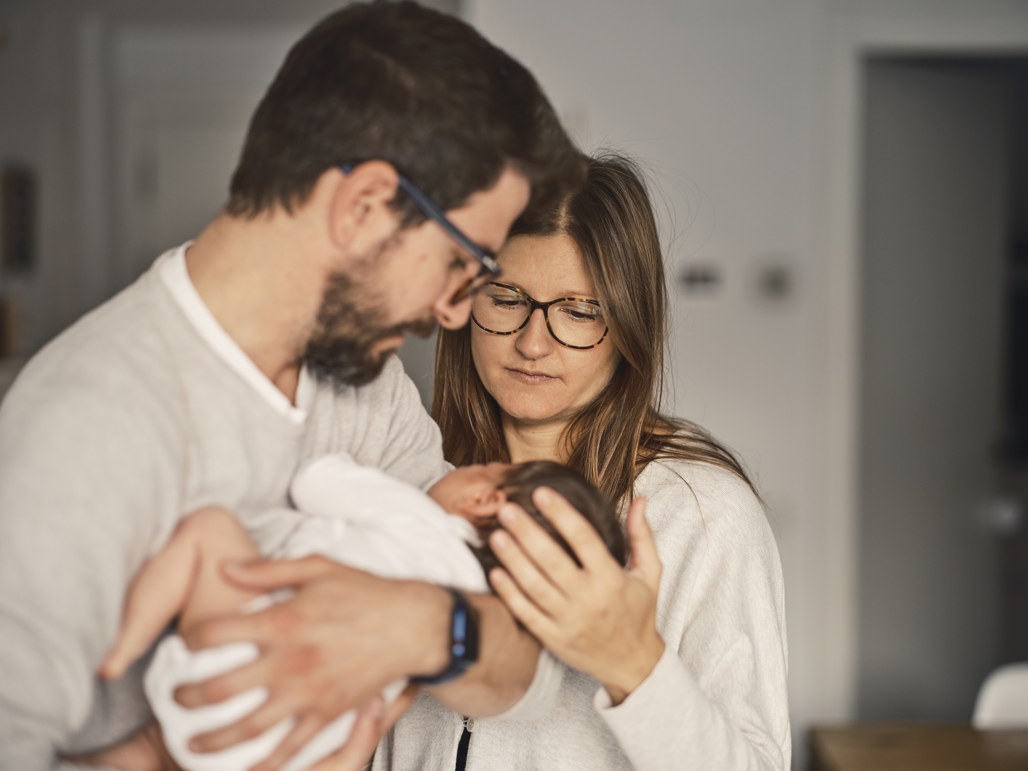 un couple regarde avec intensité un nourrisson dans les bras de l'homme