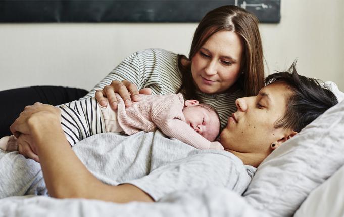 un bébé dort sur le torse de son papa, la maman a la main posée sur lui