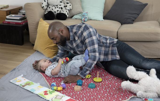 un papa joue avec un bébé par terre devant le canapé
