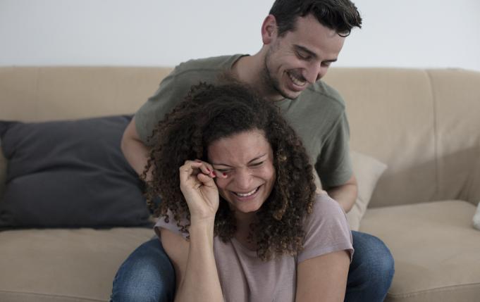 une femme rit et pleure en même temps, son compagnon est à côté d'elle
