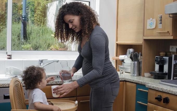 une femme enceinte sert un verre d'eau du robinet à sa petite fille