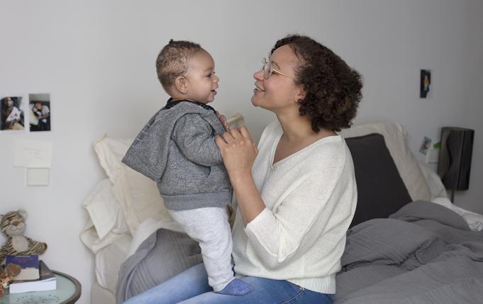 Une jeune maman joue avec son bébé debout sur ses genoux