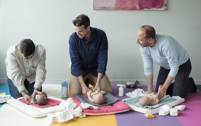 trois hommes dans un atelier de futurs papas apprennent à changer une couche sur des baigneurs