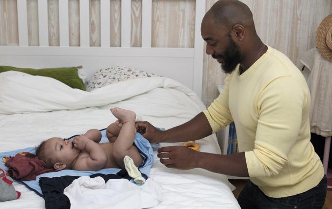 un père change la couche de son bébé sur un lit