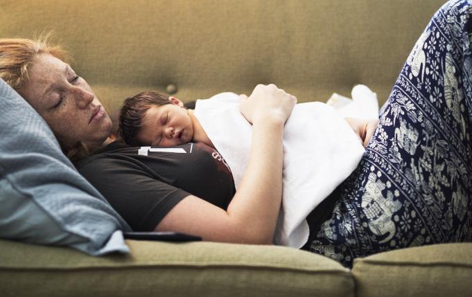 un nourrisson dort sur sa maman qui se repose aussi sur le canapé