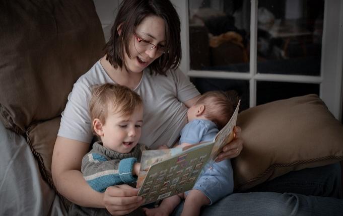 une femme allaite un bébé tout en lisant un livre à un enfant