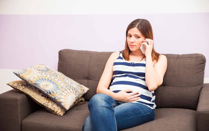 Une femme enceinte est au téléphone, assise sur son canapé