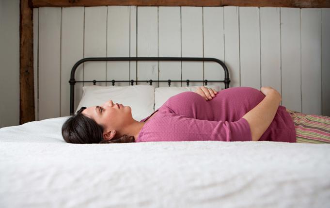 Une femme enceinte est allongée sur le dos sur son lit