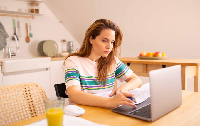 une femme chez elle devant des papiers et un ordinateur