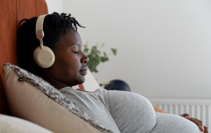 une femme enceinte semi-allongée avec un casque sur les oreilles