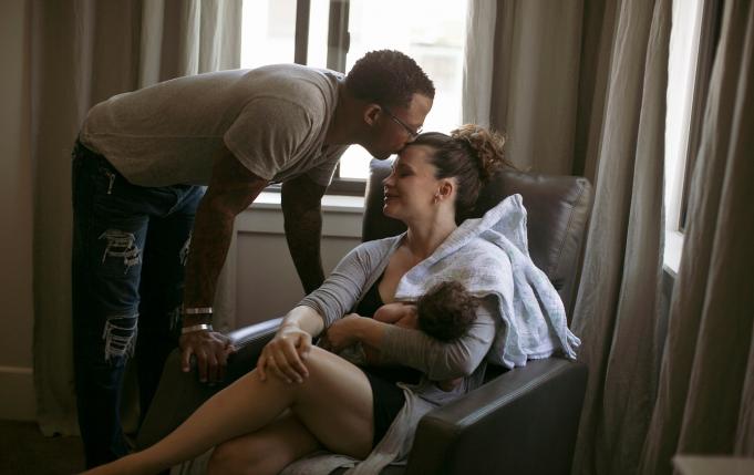 un homme embrasse le front d'une femme en train d'allaiter son nourrisson