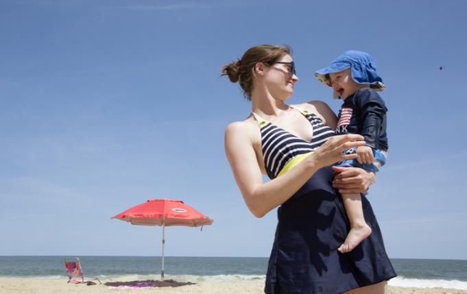 un bébé à la plage avec chapeau, vêtements couvrants et parasol