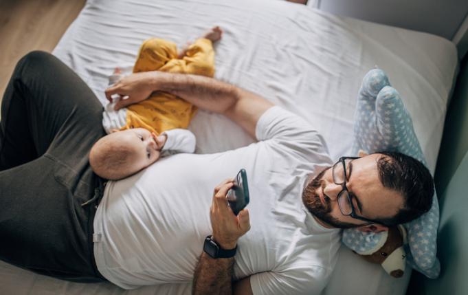 un papa regarde son smartphone alors que son bébé cherche à interagir avec lui