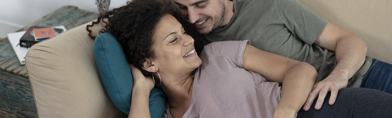 Une femme enceinte et son partenaire enlacés sur un canapé