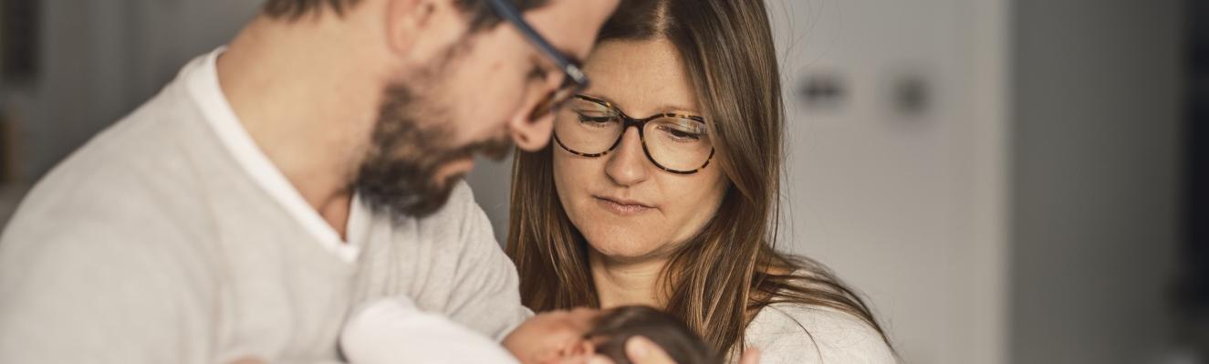 un couple regarde avec intensité un nourrisson dans les bras de l'homme
