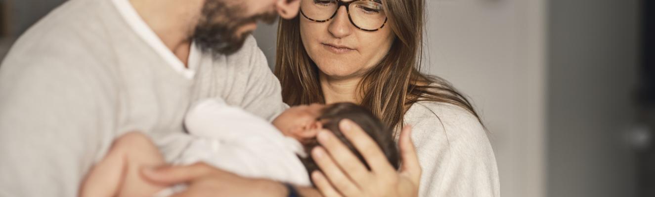 un couple regarde avec intensité un nourrisson dans les bras de l'homme