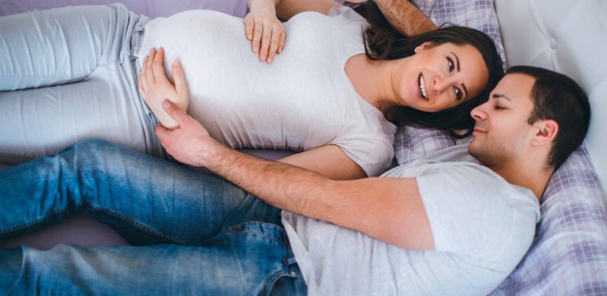 Une femme enceinte et son partenaire enlacés sur un lit