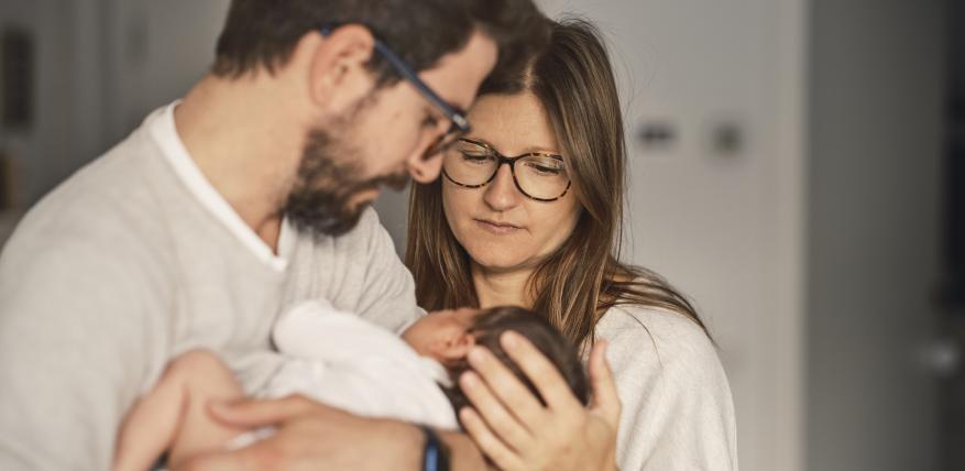 un couple regarde avec intensité un nourrisson dans les bras de l'homme