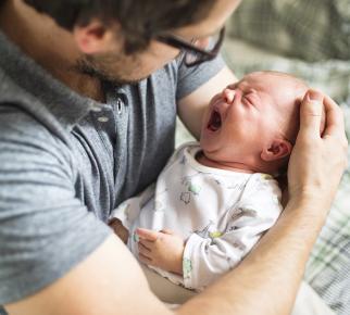 un nourrisson qui pleure dans les bras d'un homme