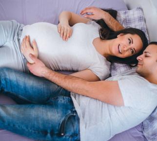 Une femme enceinte et son partenaire enlacés sur un lit