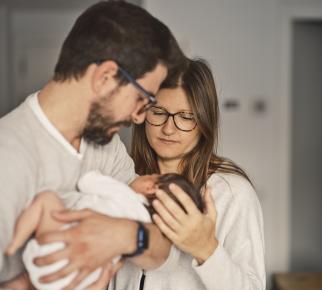 un couple regarde avec intensité un nourrisson dans les bras de l'homme