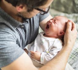 un bébé pleure très fort dans les bras d'un homme