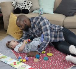 un papa joue avec un bébé par terre devant le canapé