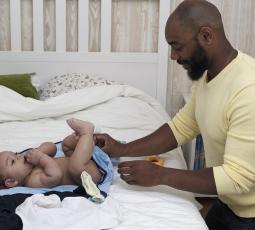 un père change la couche de son bébé sur un lit