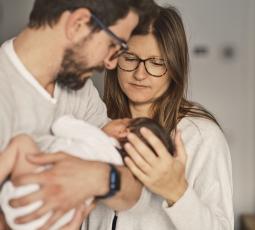 de jeunes parents regardent leur nourrisson tenu dans les bras du père