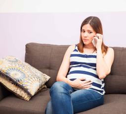 Une femme enceinte est au téléphone, assise sur son canapé