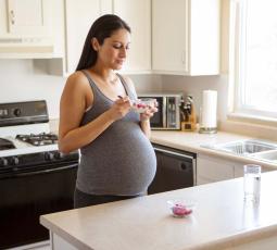 Une femme enceinte mange un fromage blanc aux fruits dans sa cuisine